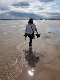 Rear view of woman walking on beach against sky