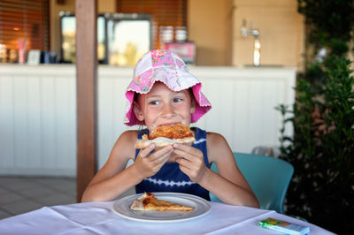 Thoughtful girl eating pizza while sitting at table in restaurant