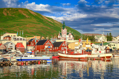 Sailboats moored on river by buildings against sky