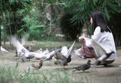Side view of woman crouching on field by birds