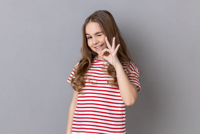 Portrait of young woman standing against gray background