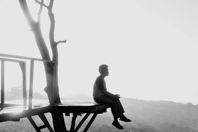 Side view of teenage boy sitting on observation point against clear sky