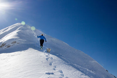 Woman with dog walking on snowcapped mountain against sky