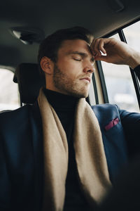 Sad businessman in suit with eyes closed sitting in taxi