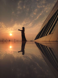 Silhouette man standing on shore against sky during sunset