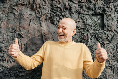 Joyful senior man giving thumbs up against textured dark wall in urban setting