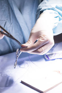 Midsection of surgeon cutting thread on table