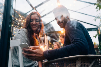 Low angle view of young friends using smart phone in glass cabin