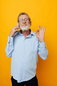 Senior man talking on smart phone against yellow background