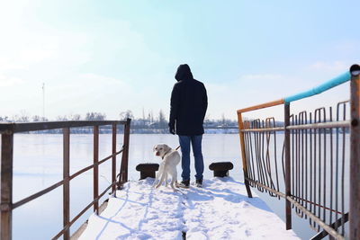 Rear view of man with dog walking in snow