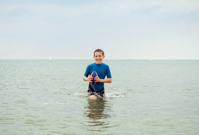 Playful boy playing with rugby ball in sea