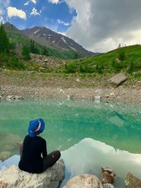 Man sitting on rock by lake against sky