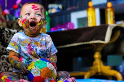 Full length of a baby boy sitting with multi coloured face.