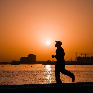 Silhouette man on beach against orange sky