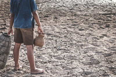 Low section of boy holding containers while standing on cracked field