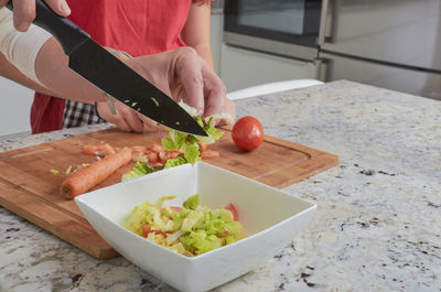 Close-up of mother and daughter preparing salad in kitchen at home