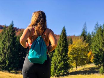 Young woman standing amidst trees against clear blue sky
