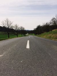 Empty road by bare trees against sky