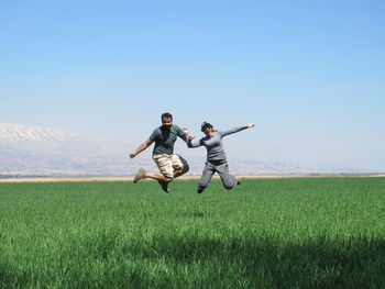 Full length of couple jumping on field against clear sky