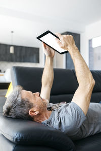 Mature man using digital tablet while lying down on sofa at living room