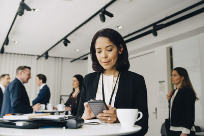 Female business person using phone while standing at table in office workplace