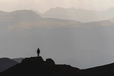 Silhouette man standing on rock against sky