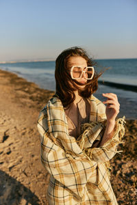 Portrait of young woman standing at beach against sky