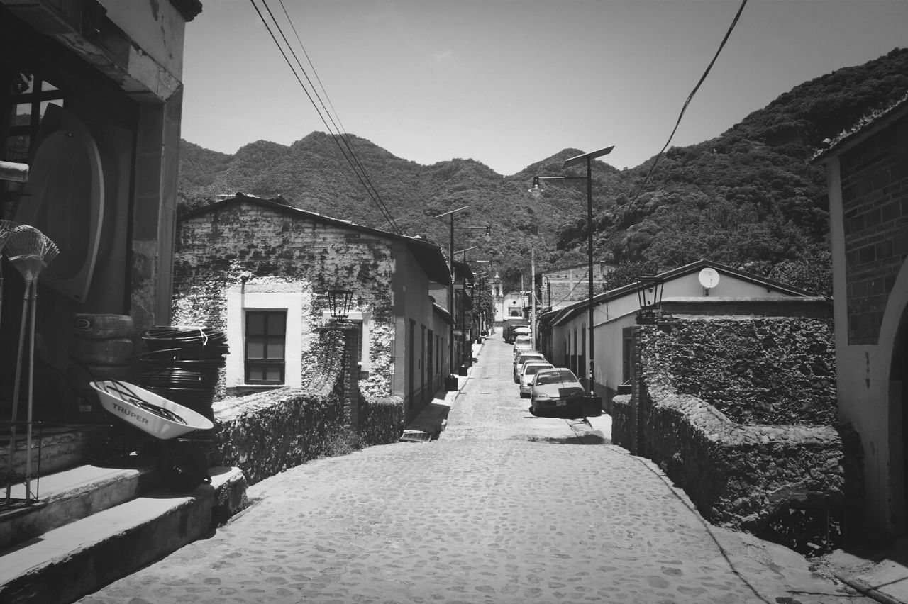 built structure, architecture, building exterior, house, mountain, power line, the way forward, sky, electricity pylon, residential structure, cable, residential building, clear sky, electricity, town, transportation, power supply, street, day, village