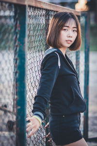 Portrait of smiling woman standing by chainlink fence