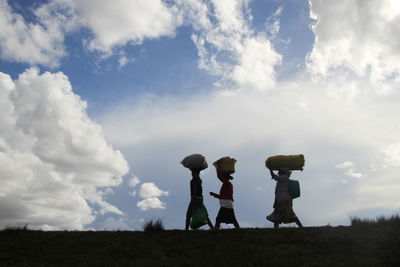 Rear view of people standing on field against sky