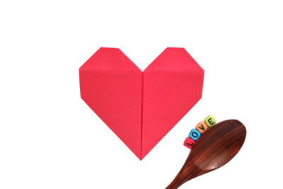 Directly above shot of red heart shape by blocks and spoon on white background