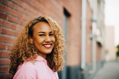 Side view portrait of young woman with curly hair against brick wall