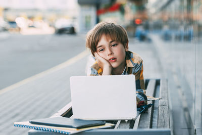 A thoughtful boy is lying on a bench and preparing for school lessons, next to a backpack. 