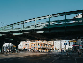 People on bridge in city against clear sky