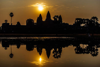 Silhouette buildings by lake against sky during sunset