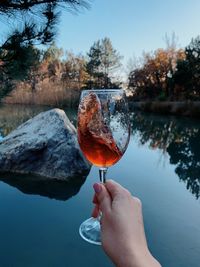 Person holding wineglass against lake