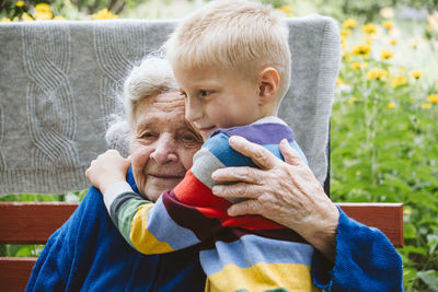Grandmother embracing grandson while sitting on bench outdoors