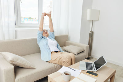 Young woman using digital tablet while sitting on sofa at home