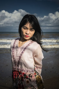 Young woman standing at beach against sky