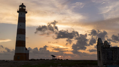 Lighthouse by sea against sky during sunset