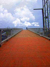 Walkway leading to sea against cloudy sky