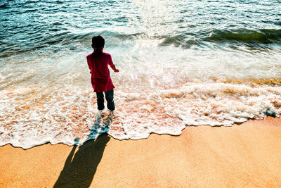 High angle view of boy standing amidst surf on shore at beach