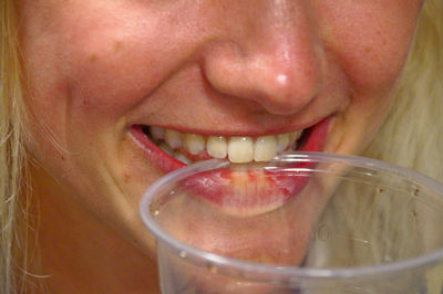 Close-up of smiling young woman holding plastic glass in mouth