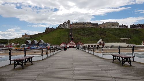 People on bench by building against cloudy sky