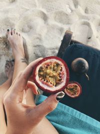 Low section of woman holding passion fruit at beach