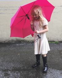 Happy girl with pink umbrella standing on wet street