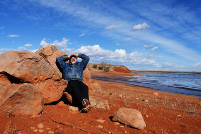 Rear view of woman sitting on rock against sky