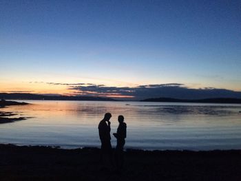 Silhouette couple standing at beach against sky during sunset