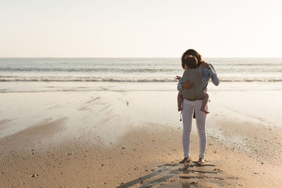 Mother carrying son while standing at beach