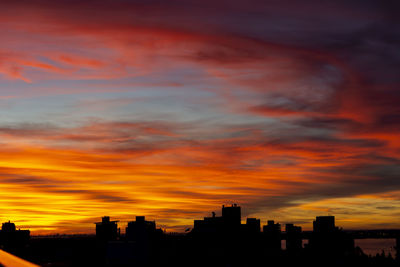 Silhouette buildings against dramatic sky during sunset